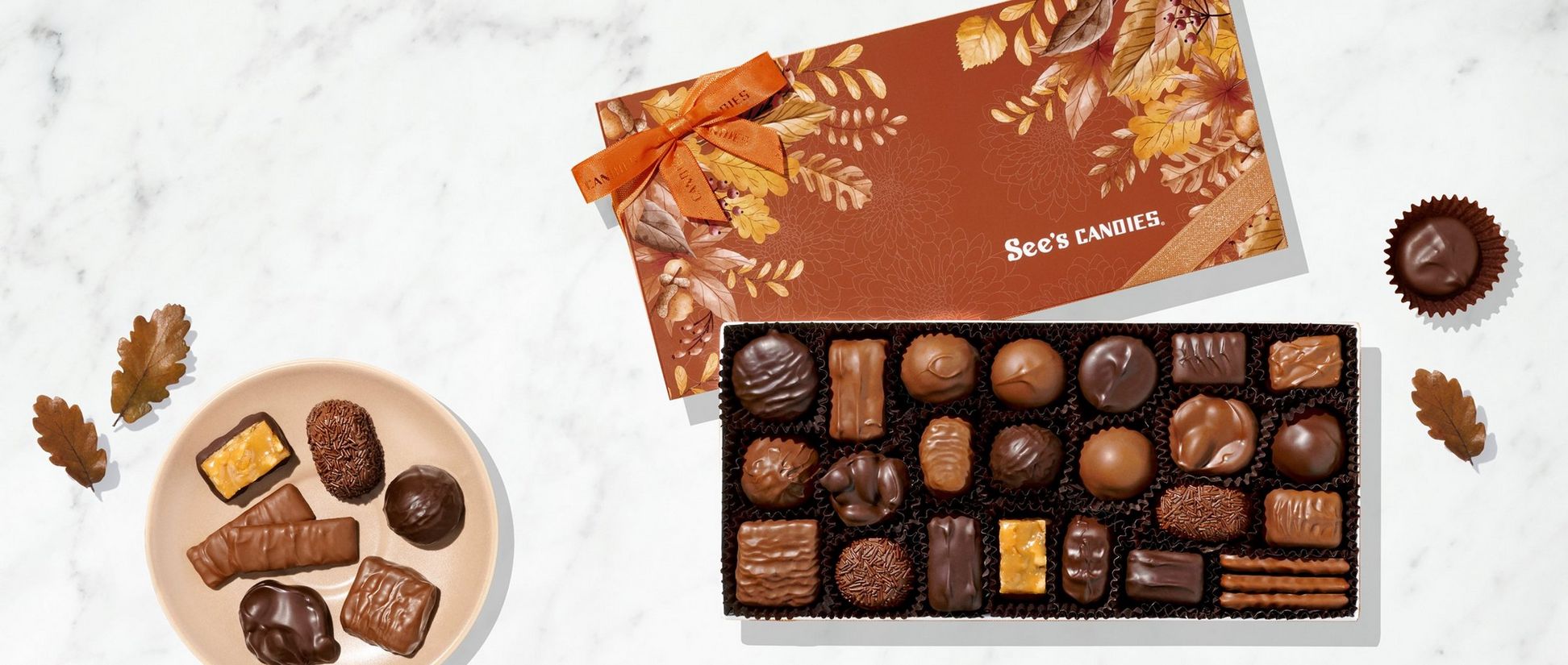A box of assorted chocolates with a fall themed lid on a marble background