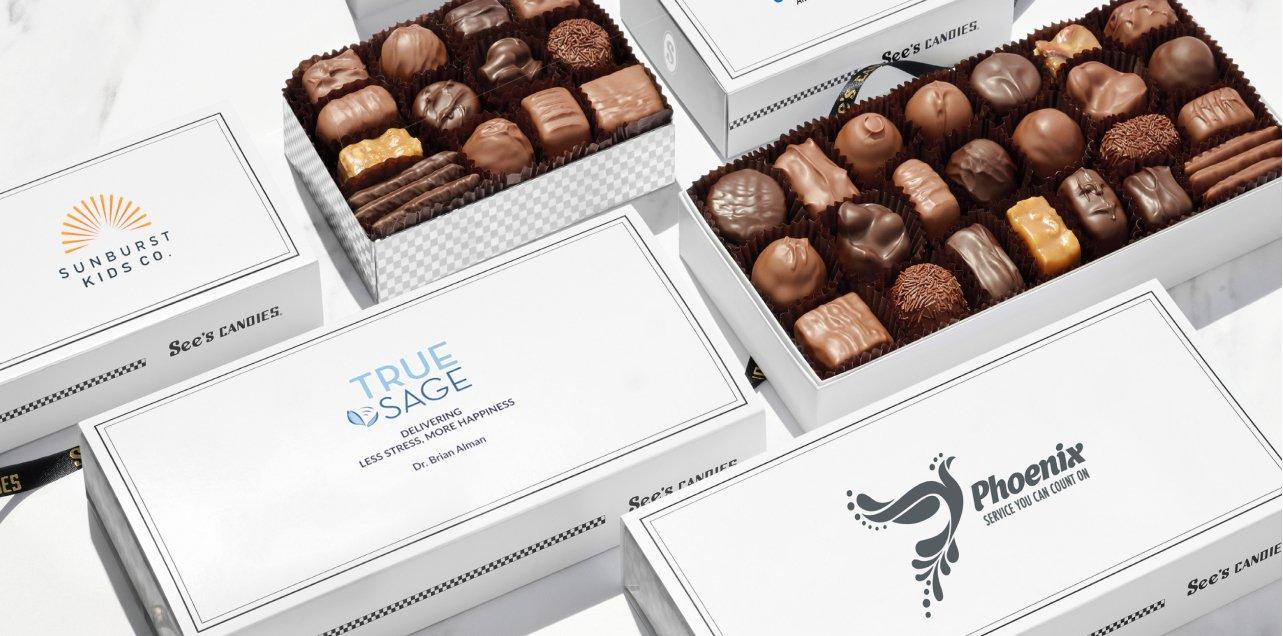 Boxes of See's Candies chocolate with company logos on the box for corporate gifting