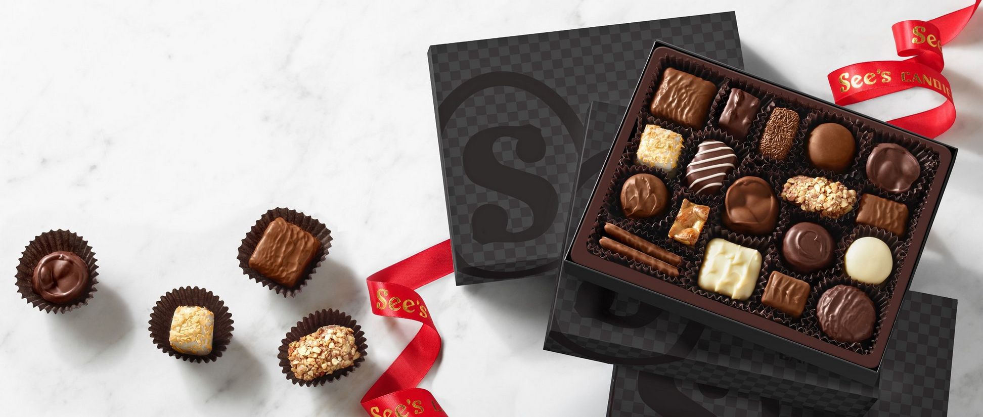 A black tonal checker box with a See's emblem filled with chocolate