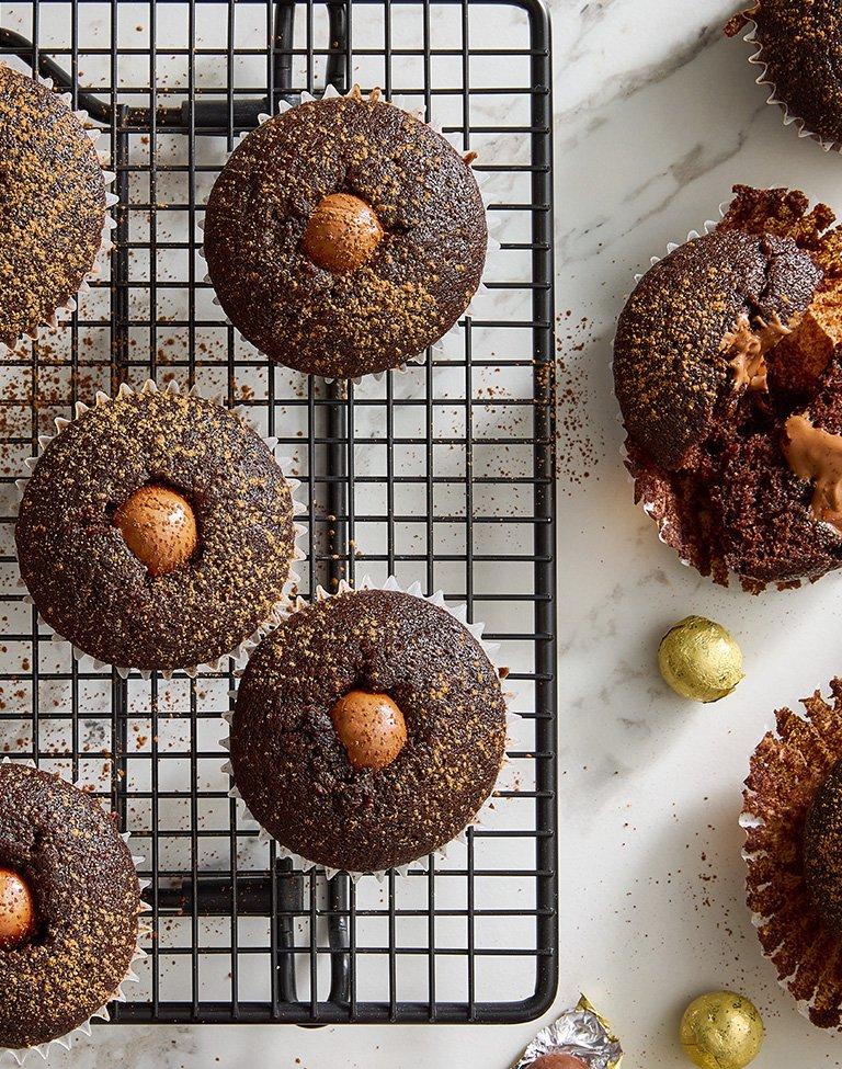 Multiple chocolate lava cupcakes with a See's Milk Chocolate Ball in the middle placed on a cooling rack 