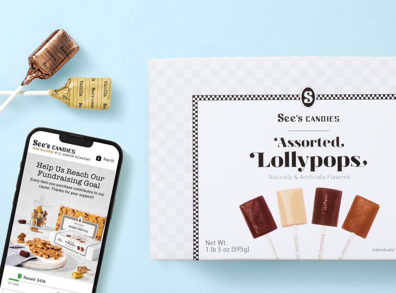 A phone screen on the See's Candies Yumraising page next to a box of Lollypops