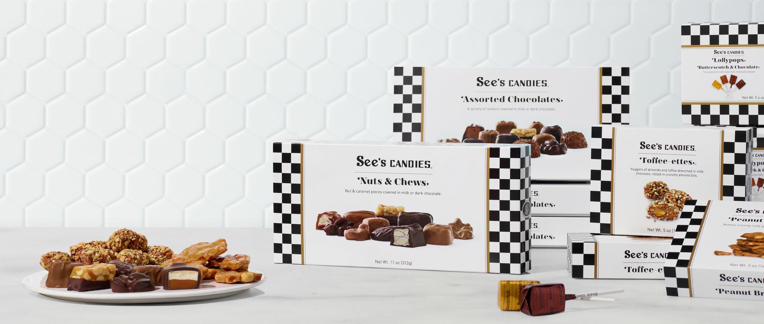 Boxes of chocolate and candies are seen against a white tile background. A candy dish filled with chocolate pieces sits in front.