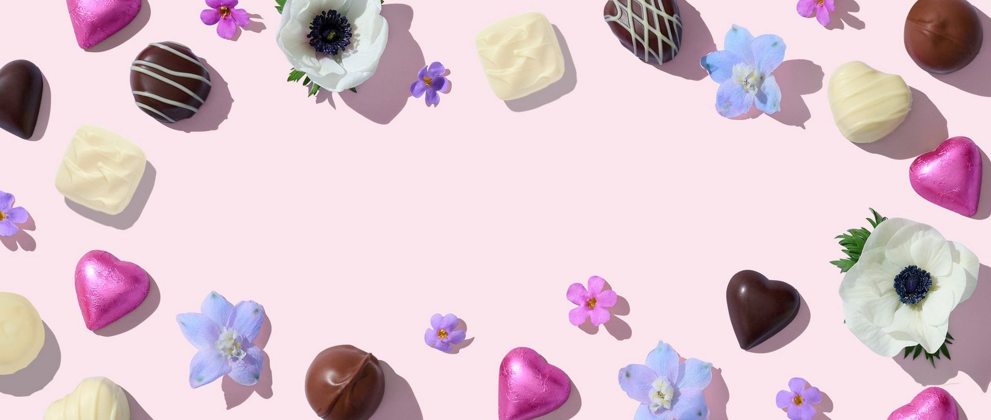 A border of chocolates and colorful flowers on a light pink background