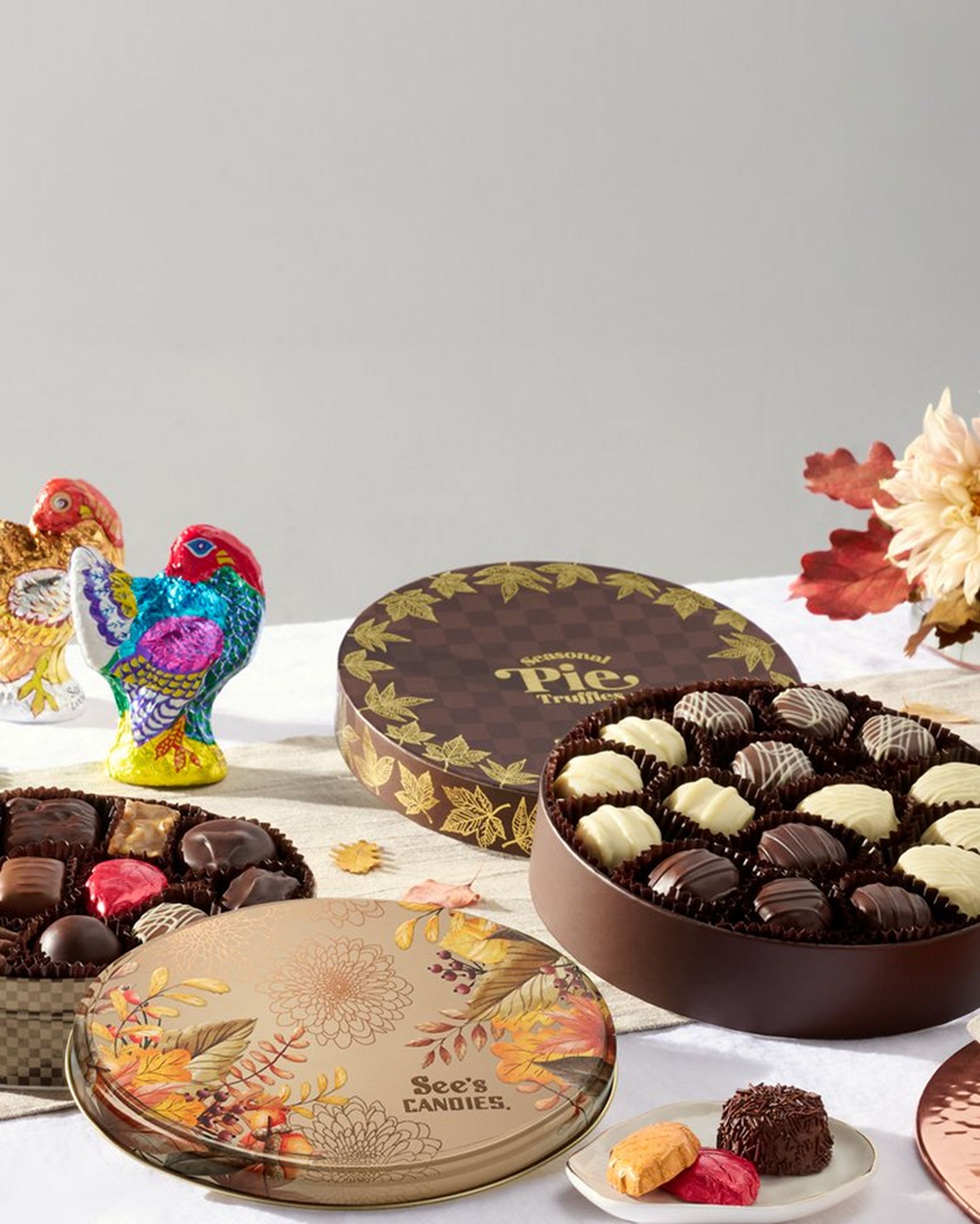 A fall tablescape featuring round chocolate boxes with autumnal designs next to two chocolate turkeys