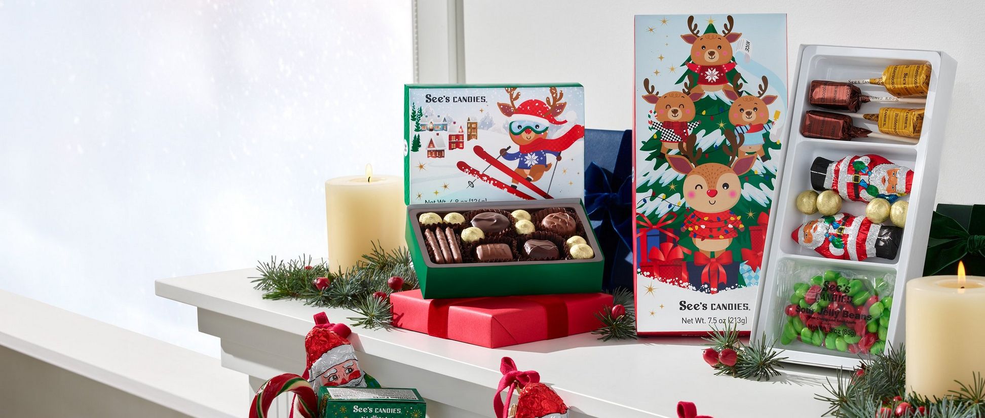 Opened boxes of See's Candies decorated with cartoon reindeer designs sit on top of a mantle.