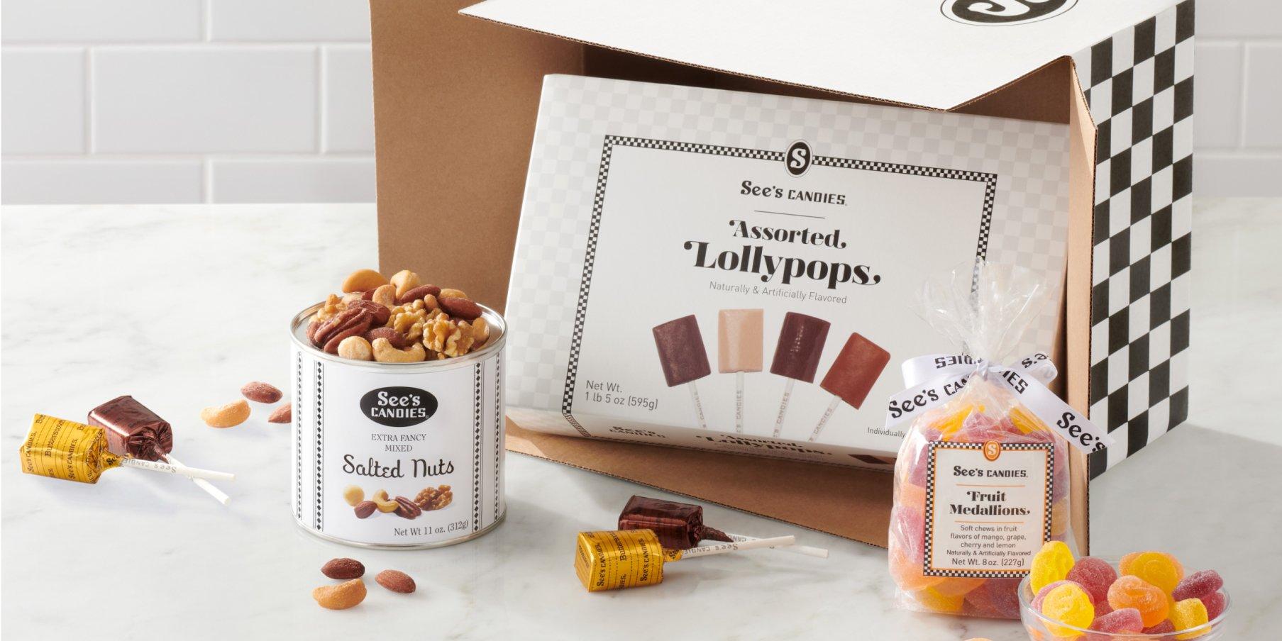 An assortment of treats including salted nuts, assorted lollypops, and fruit medallions coming out of a shipping box