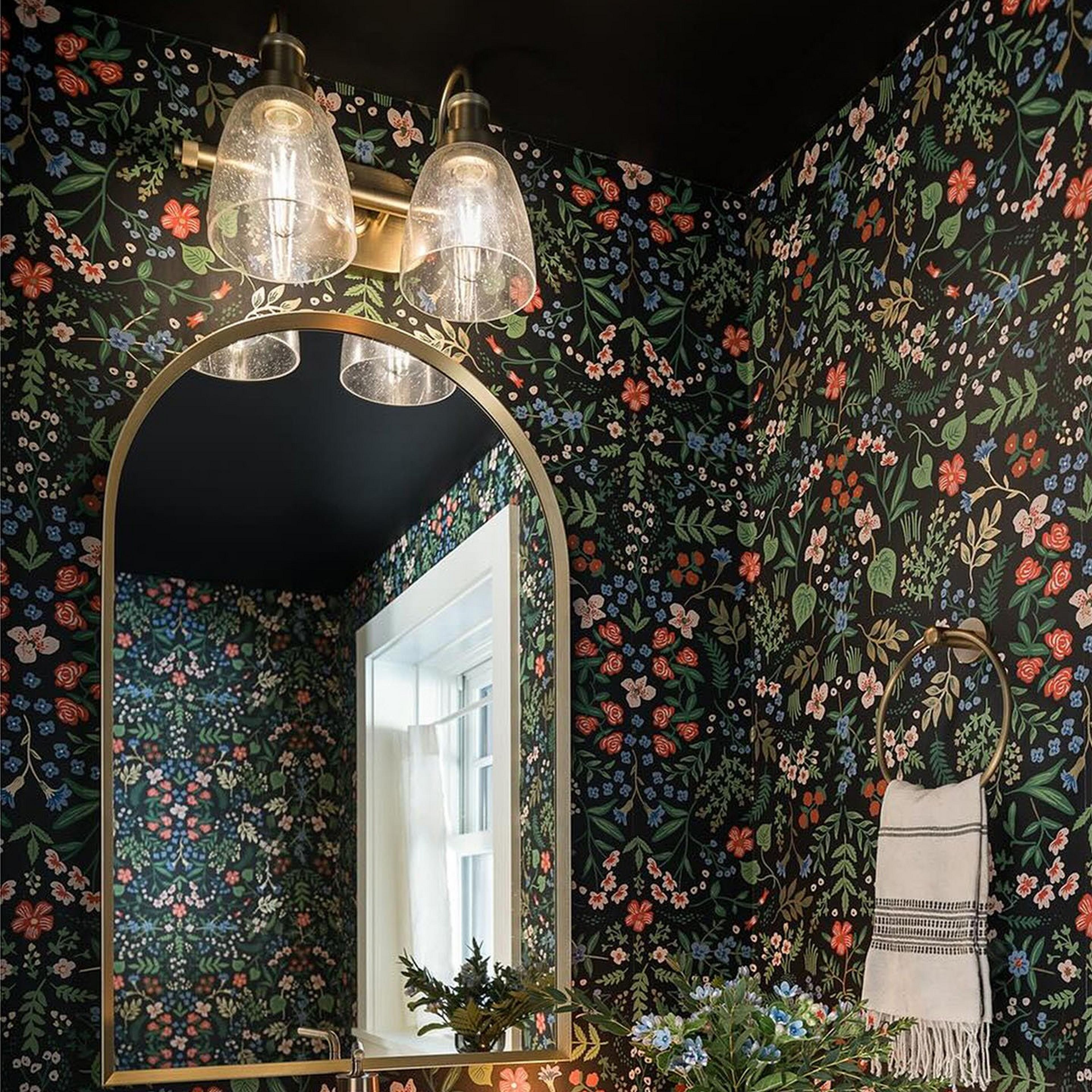 Versatile vanity light over an arched mirror in a bathroom with dark, floral wallpaper