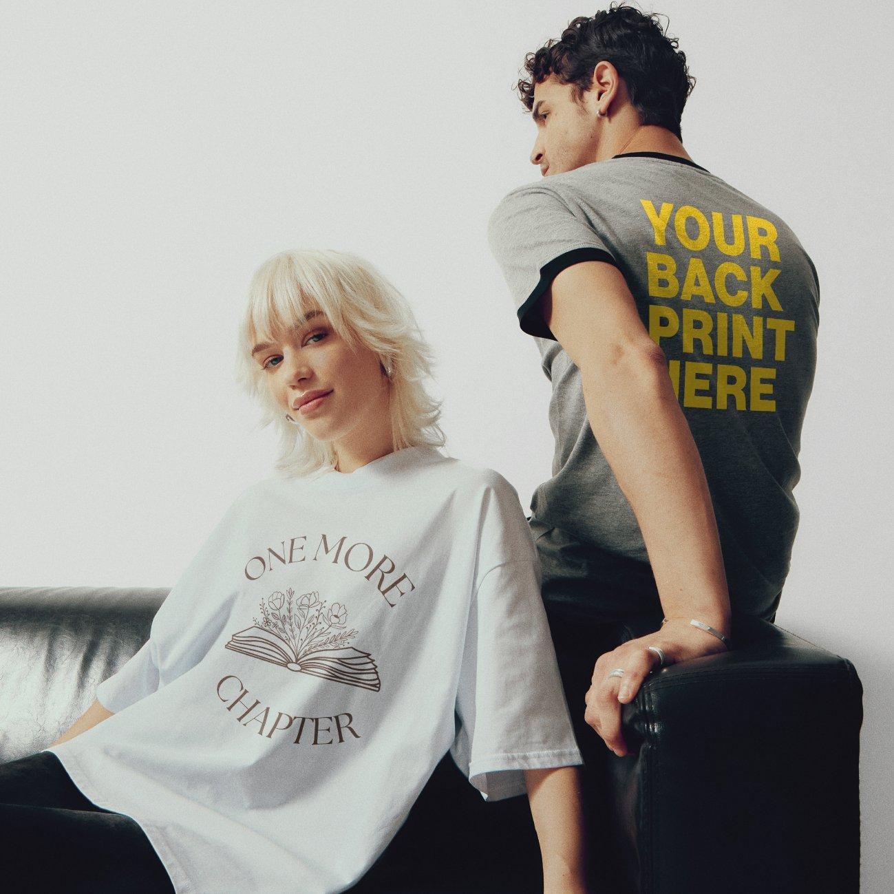 Una mujer lleva una camiseta blanca con motivos de libros, sentada en un sofá, al lado de un hombre con una camiseta gris y un estampado amarillo en la espalda "Tu estampado aquí".
