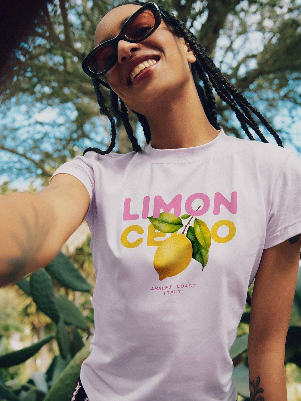 Mujer con gafas de sol sonríe a la cámara y lleva una camiseta con un limón y las palabras "Limoncello".