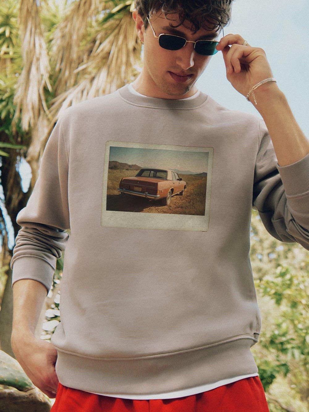 Hombre con gafas de sol mira hacia abajo y lleva una sudadera con una foto retro de un coche.