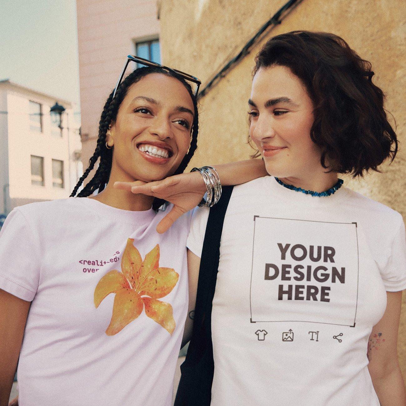 Dos chicas jóvenes en la ciudad. Una lleva el pelo oscuro y viste una camiseta rosa con un estampado floral. La otra, de pelo corto, lleva una camiseta blanca con print y letras en negro.