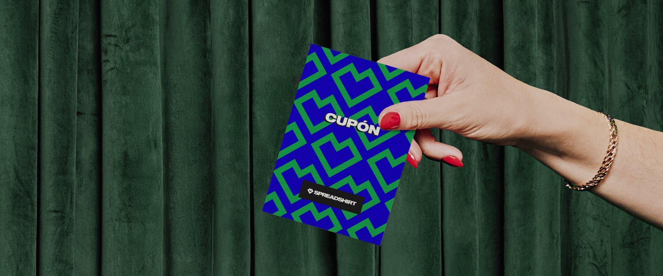 Mano con esmalte de uñas rojo sostiene un vale de Spreadshirt.