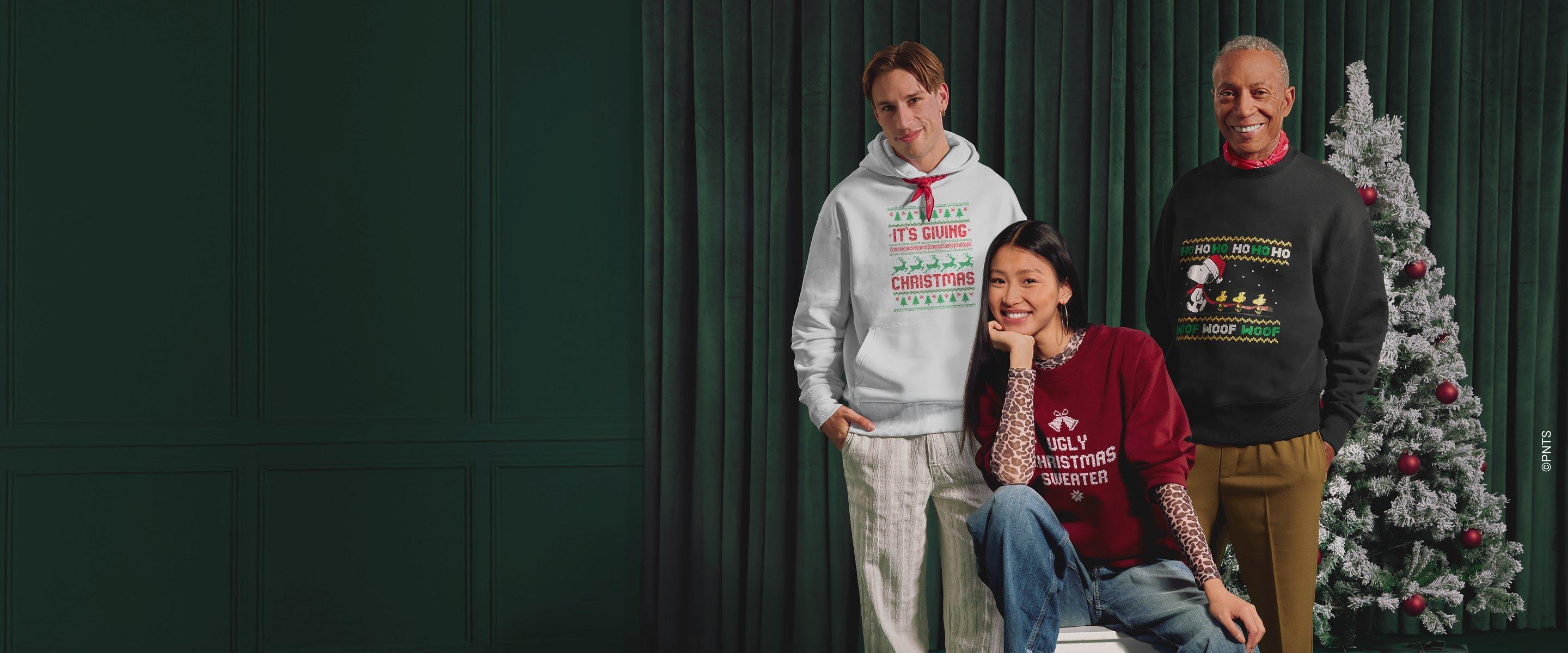 Tres personas llevan jerseys navideños con motivos y frases festivas, de pie ante un fondo verde.