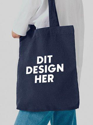 Person, der bærer en mørkeblå stofpose med hvidt tryk "Dit design her" i midten.
