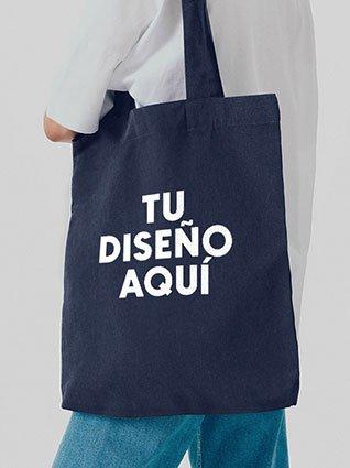 Persona de espaldas usando bolsa tote azul marino con la frase "TU DISEÑO AQUÍ" impresa en el frente