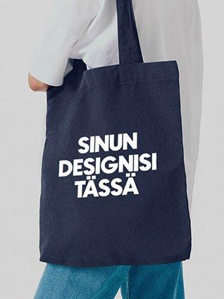 Henkilö kantaa tummansinistä kangaskassia, jossa on valkoinen ”Sinun designisi täällä” -painatus keskellä.