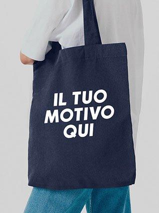 La persona porta una borsa di stoffa blu scuro con la scritta bianca "Il tuo motivo qui" al centro.