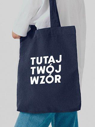 Osoba nosi ciemnoniebieską torbę z materiału, na środku której znajduje się biały nadruk „Twój wzór tutaj”.