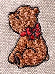 Osito bordado de color marrón con lazo rojo, sobre tela beige