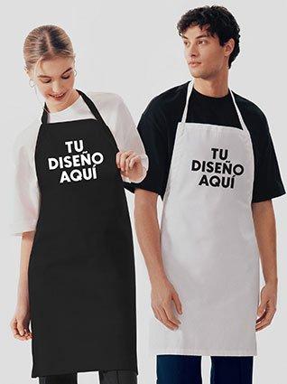 Dos personas usando delantales, una con delantal rojo y otra con delantal blanco, ambos con la frase "TU DISEÑO AQUÍ" impresa en el frente