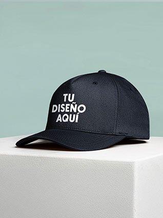 Gorra negra sobre una superficie clara con la frase "TU DISEÑO AQUÍ" impresa en el frente