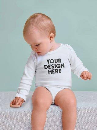 Baby in a white long-sleeved bodysuit with black print "Your design here" sitting and looking down.