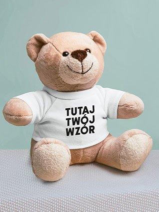 Pluszowy miś ma na sobie białą koszulkę z czarnym nadrukiem „Twój wzór tutaj”.