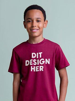 Dreng iført bordeauxrød T-shirt med hvidt tryk "Dit design her" og smilende.