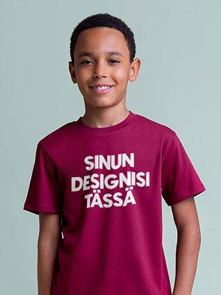 Poika yllään viininpunainen t-paita, jossa valkoinen painatus ”Sinun designisi täällä” ja hymyilee.