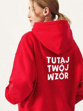 Kobieta od tyłu w czerwonej bluza z kapturem, z białym nadrukiem „Twój wzór tutaj” na plecach.