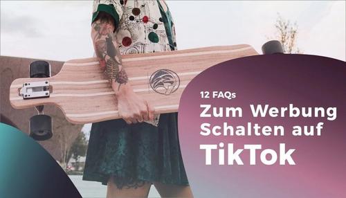 Tättowierte Person in buntem Hemd und Rock hält ein hölzernes Longboard unter dem Arm.