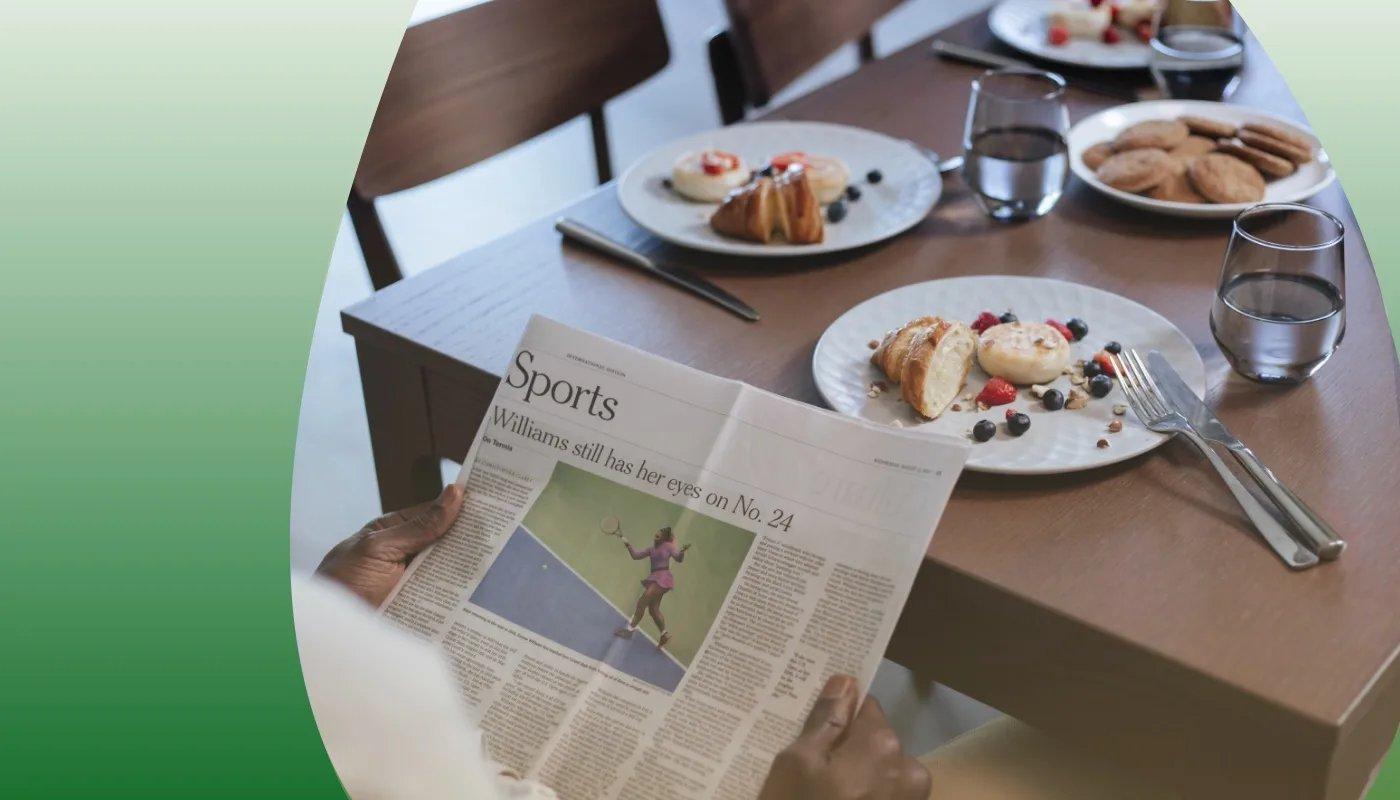 Person an Frühstückstisch liest Sportteil der Zeitung.