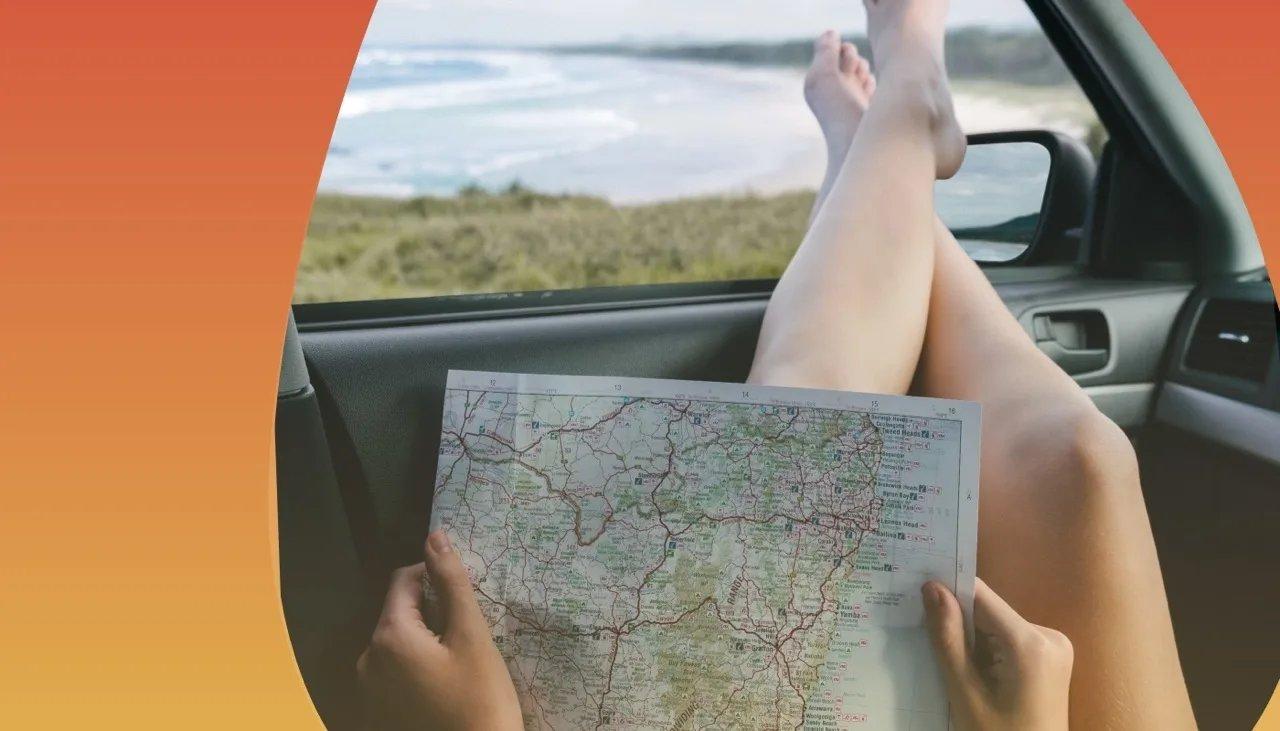 Person streckt entspannt Füße zum Autofenster heraus und studiert eine Landkarte.