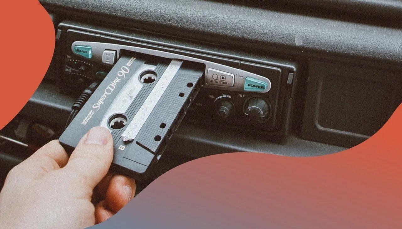 Eine Hand legt eine Kassette in ein Autoradio ein.