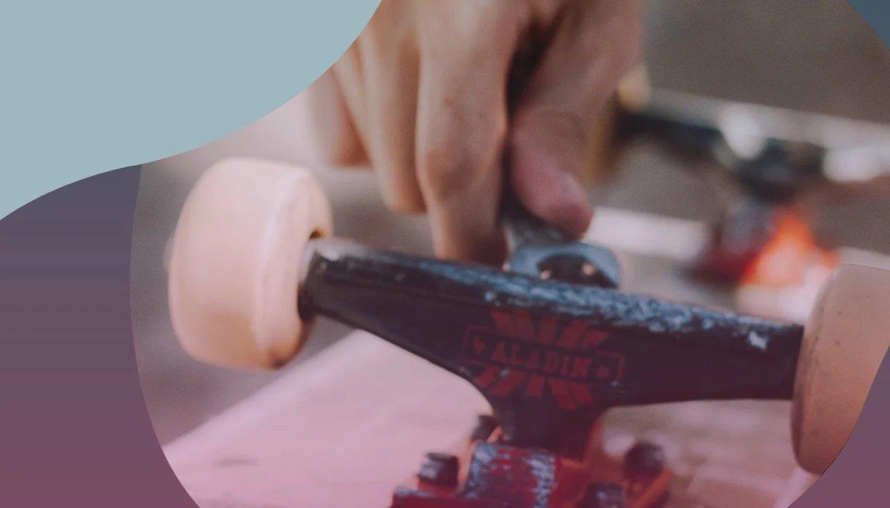 Detail einer Hand, die eine Schraube an der Skateboardunterseite festzieht.