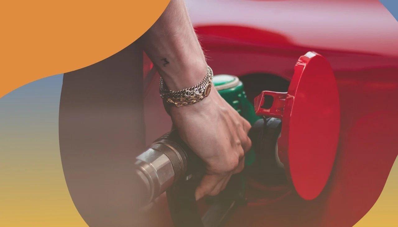 Detail eines Tankdeckels eines roten Autos an der Tankstelle, das gerade aufgetankt wird.