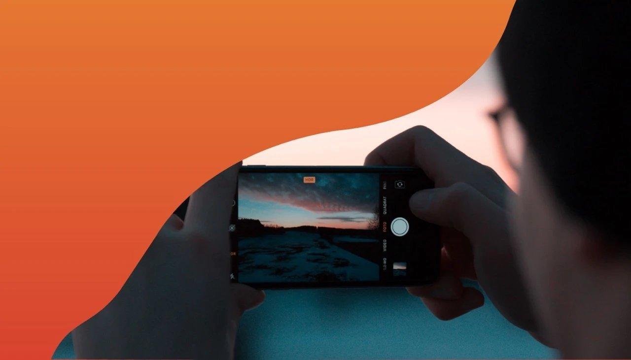 Person fotografiert Sonnenuntergang und gefärbten Himmel mit dem Smartphone.