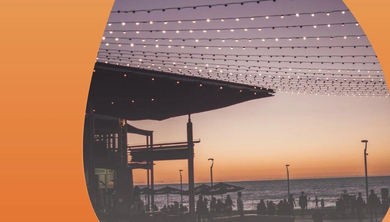 Strandbar bei Sonnenuntergang mit vielen Lichterketten, die als Himmelsdach gespannt sind.