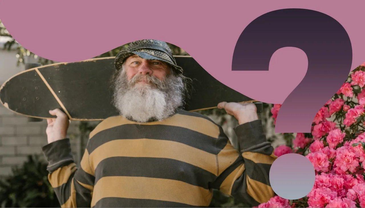 Alter weißer Mann mit langem Bart, Mütze und gelb schwarz gestreiften Oberteil hält ein Longboard hinter seinem Kopf und schaut direkt in die Kamera.