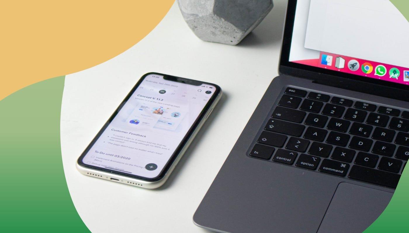 Smartphone mit geöffneter App liegt neben einem Laptop auf einem weißen Tisch, Fokus auf digitales Arbeiten.