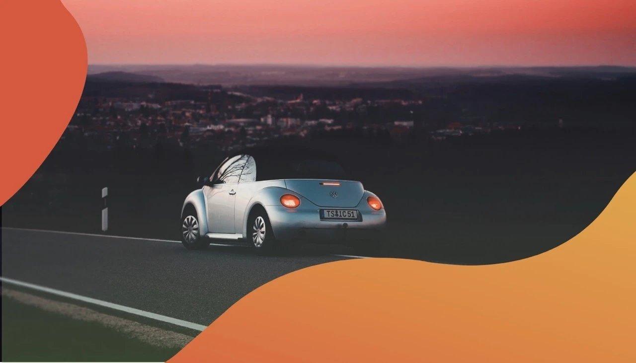 Ein VW Cabrio fährt zu Sonnenuntergang über eine verlassene Straße.