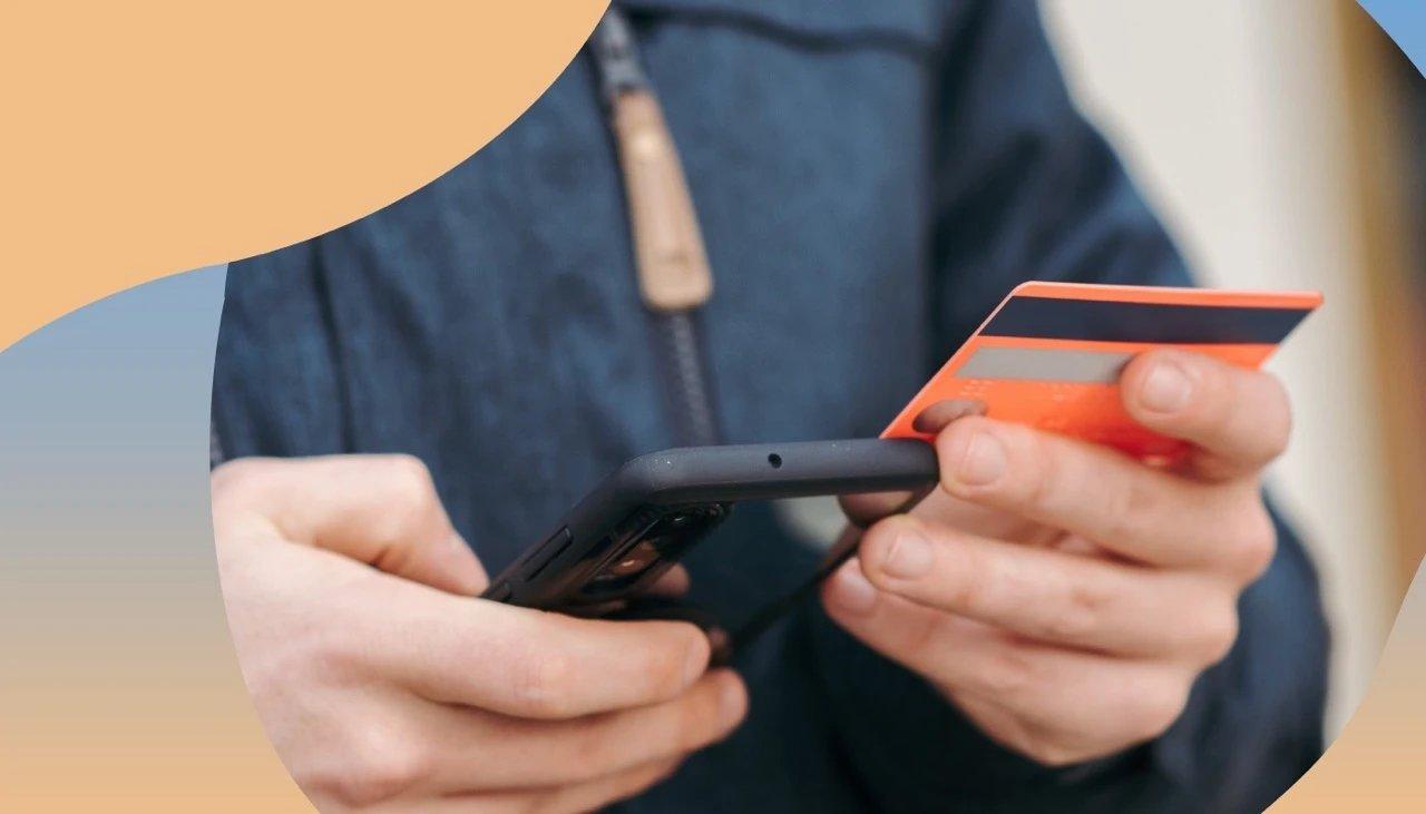 Aufnahme einer Person, die in der einen Hand eine EC-Karte hält und in der Anderen das Smartphone.