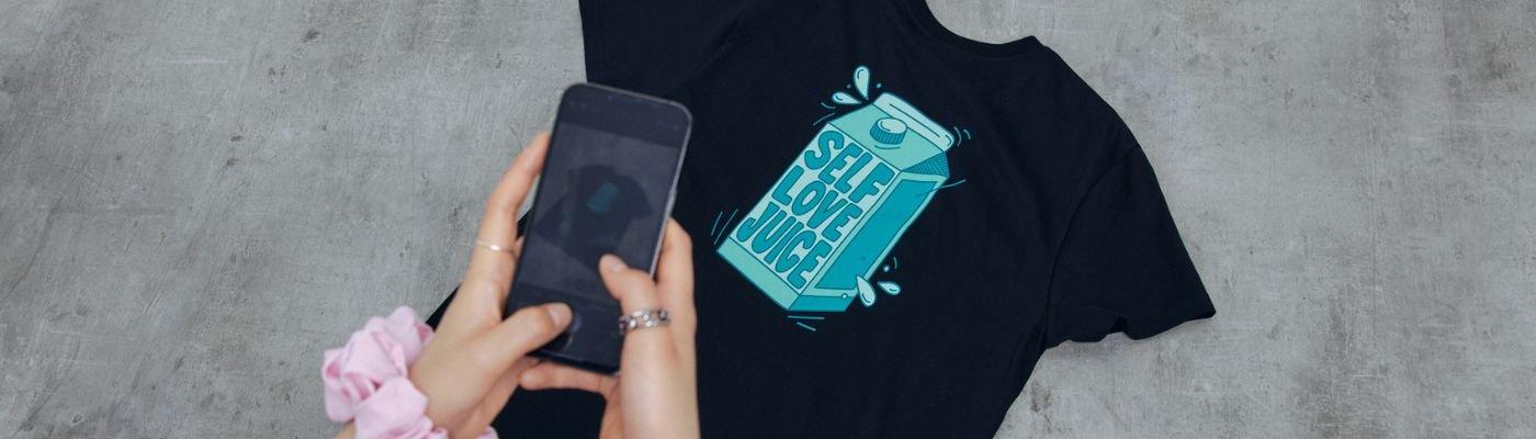 flat lay of t-shirt with someone taking a photo to illustrate how to sell t-shirts online