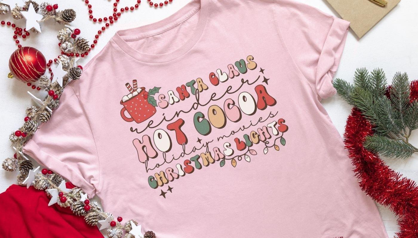 Holiday t-shirt with festive hot cocoa typography design laid out with seasonal decor