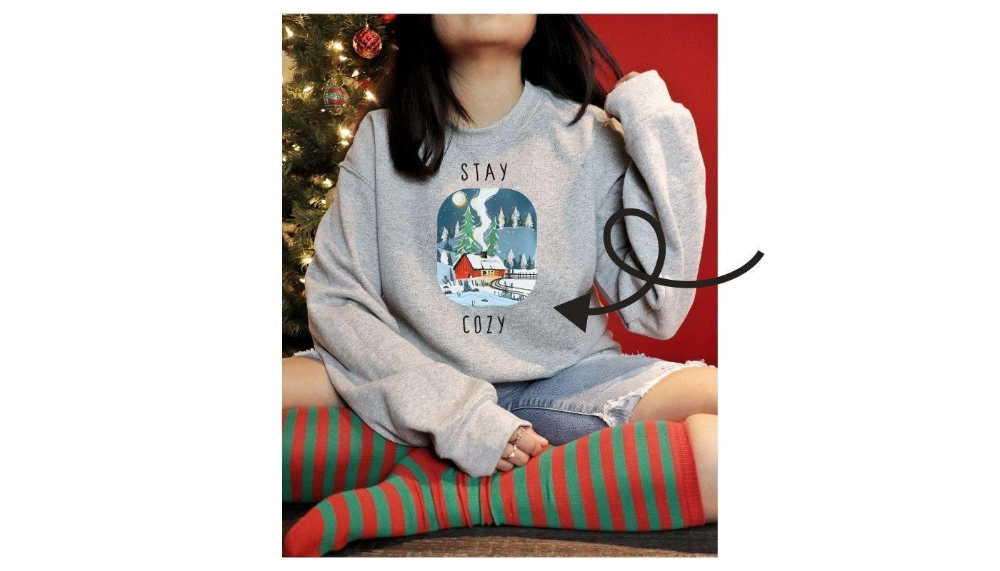 Person wearing a gray holiday sweatshirt with a cozy winter scene design, styled for Christmas content.
