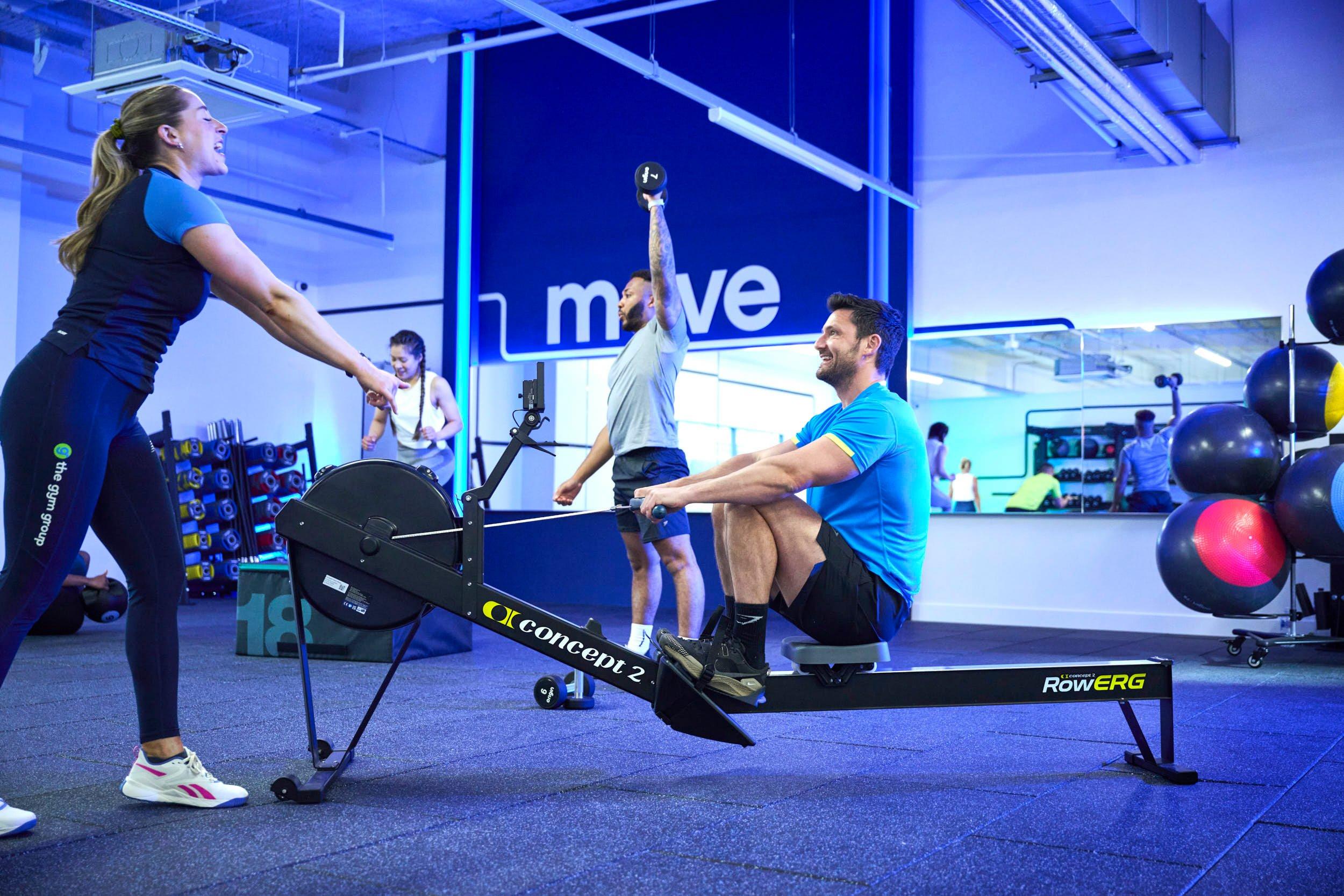 member rowing at a gym cardio class with a personal trainer