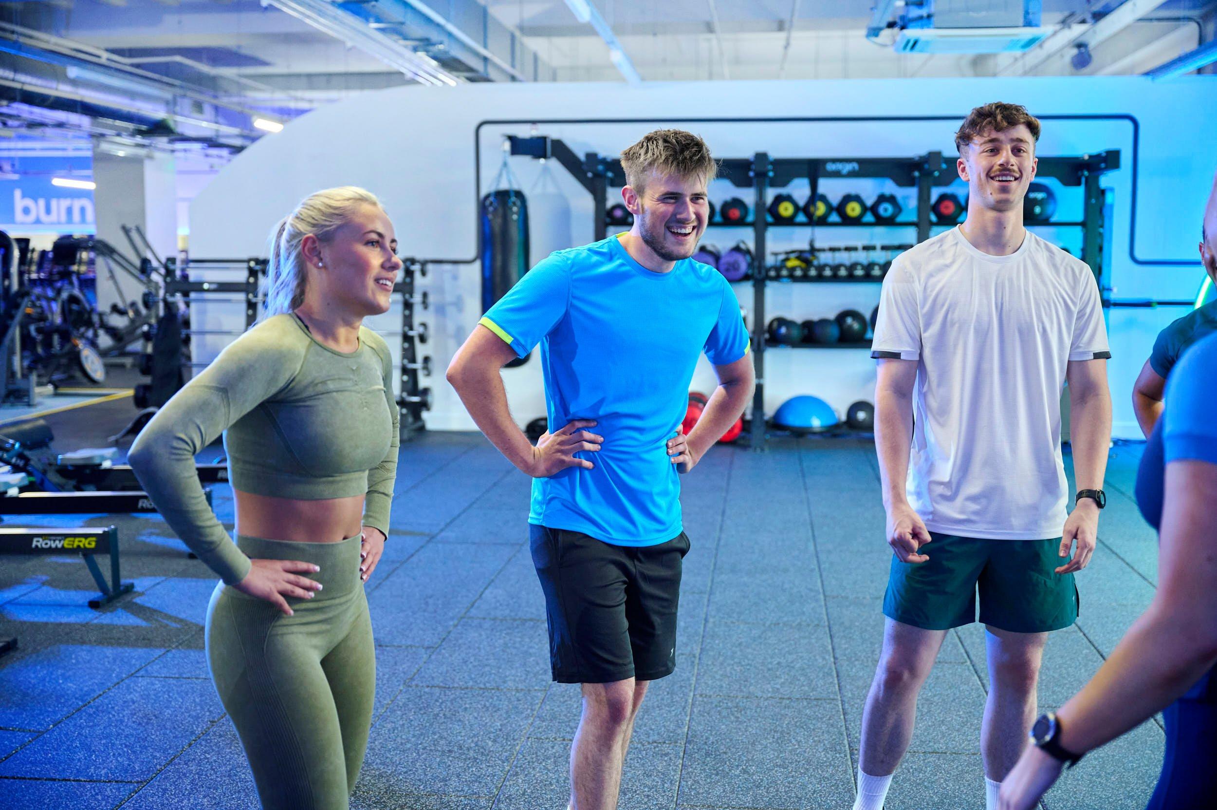 Group of gym members listening to a personal trainer's advice.