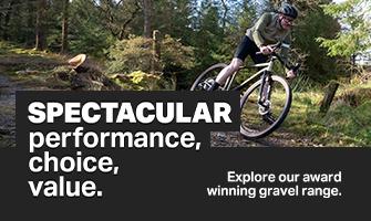 A person riding a gravel bike on a winding dirt path through a lush, green forest.