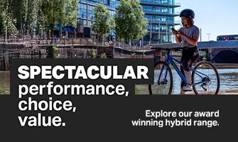 A woman in a helmet paused on her blue hybrid bike in a city setting, looking at her phone.