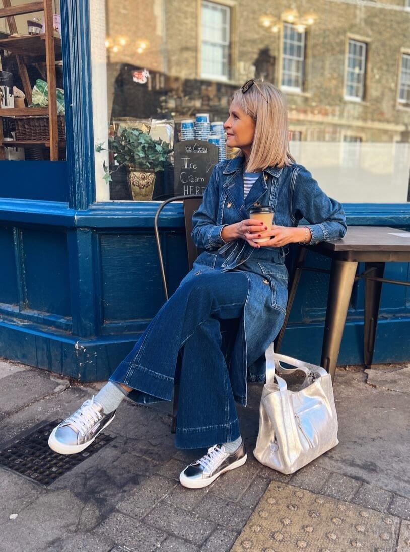 a woman sitting outside a cafe with a coffee and a bag